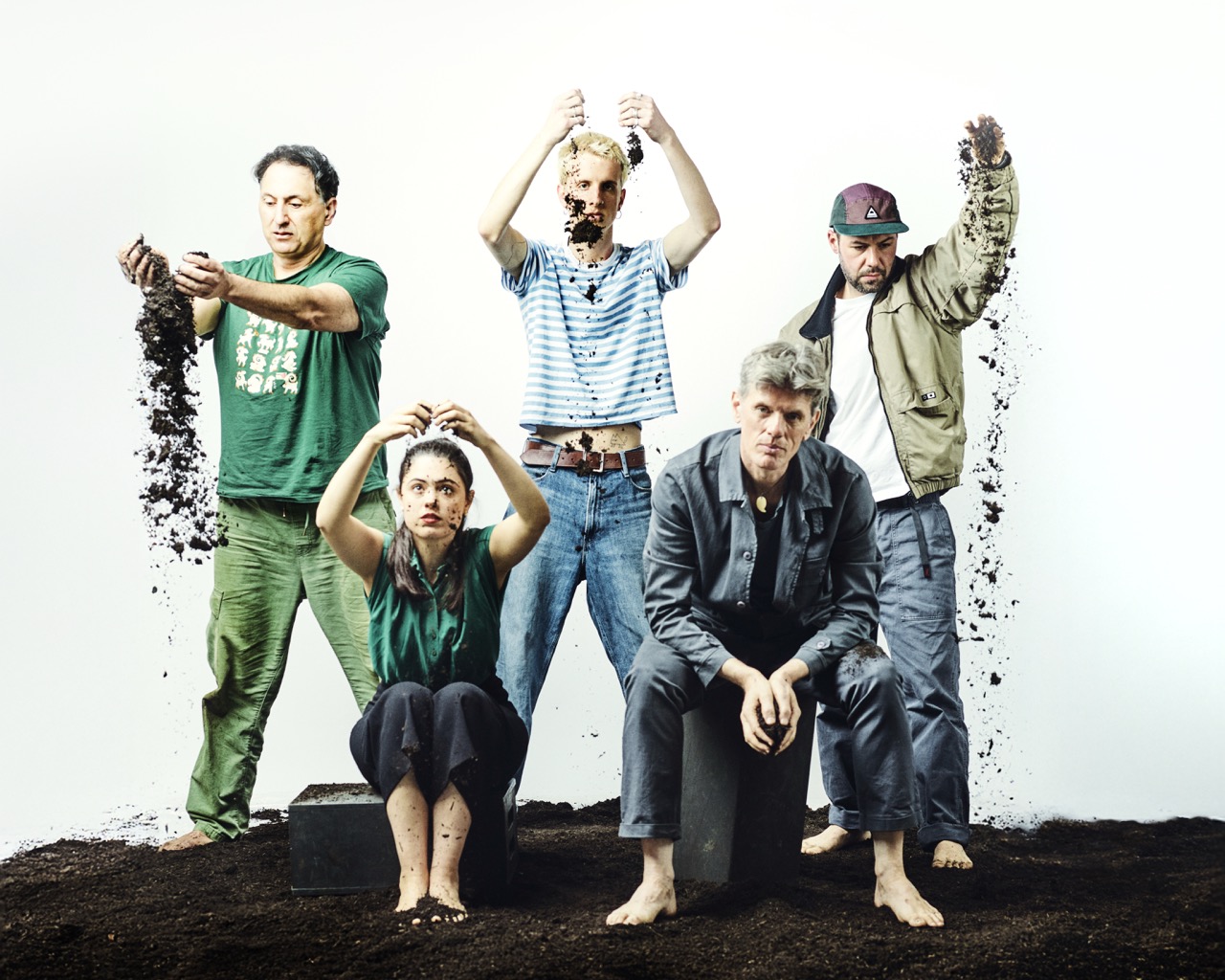 Mitglieder der Band Soil Music Collective sitzen inmitten von schwarzer Erde vor weißem Hintergrund